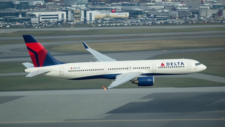 Delta airplane flying over airport tarmac.