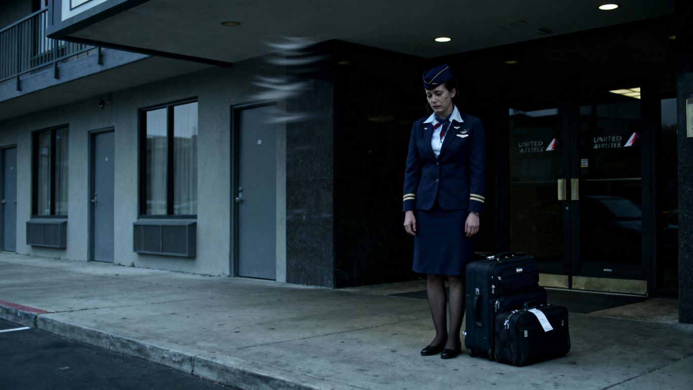 Flight attendant outside unwelcoming hotel with luggage.